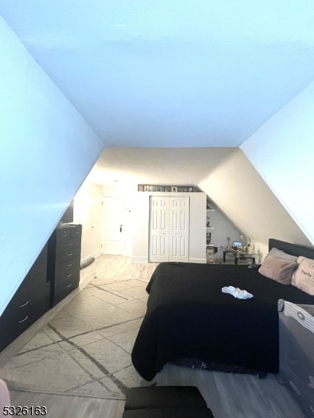 bedroom featuring light hardwood / wood-style floors, vaulted ceiling, and a closet