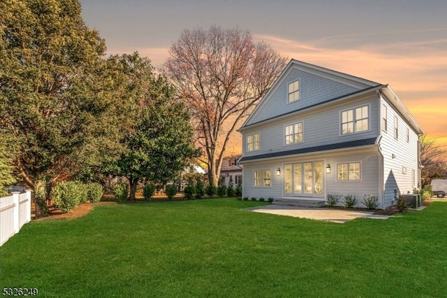 back house at dusk with a patio, cooling unit, and a lawn