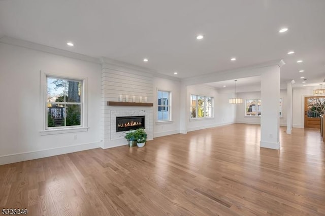 unfurnished living room with a fireplace, ornamental molding, light hardwood / wood-style floors, and a healthy amount of sunlight