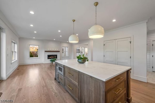 kitchen with a fireplace, light wood-type flooring, stainless steel microwave, and ornamental molding