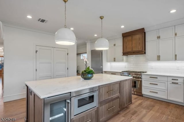 kitchen with high end appliances, beverage cooler, white cabinets, a center island, and hanging light fixtures