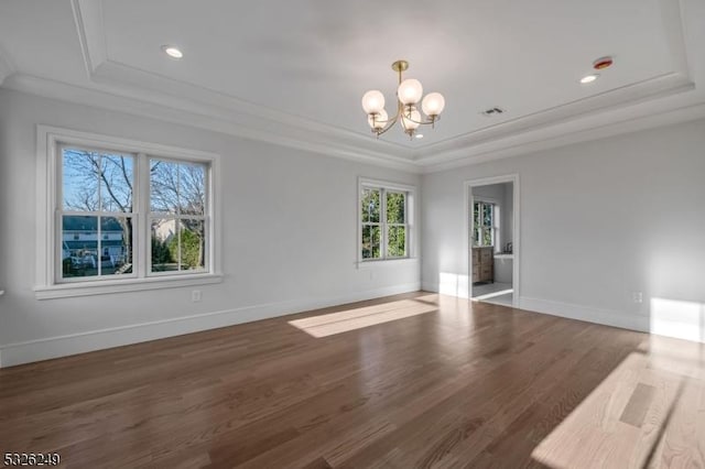 spare room with a notable chandelier, ornamental molding, dark wood-type flooring, and a tray ceiling