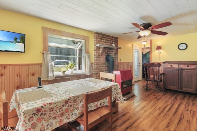 dining space with hardwood / wood-style floors, a wood stove, wooden walls, ceiling fan, and wood ceiling