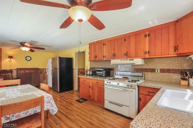 kitchen featuring backsplash, sink, light hardwood / wood-style flooring, stainless steel refrigerator, and white gas stove