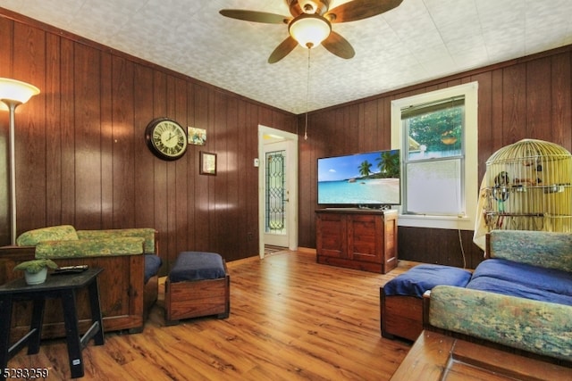 living room featuring wood-type flooring, ceiling fan, and wooden walls