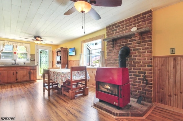 dining space with hardwood / wood-style flooring, a wood stove, sink, and wooden walls