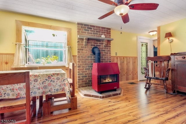 sitting room with wood-type flooring, a wood stove, ceiling fan, and wood walls