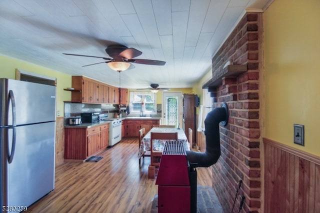 kitchen featuring ceiling fan, white range, stainless steel fridge, light hardwood / wood-style floors, and wooden walls