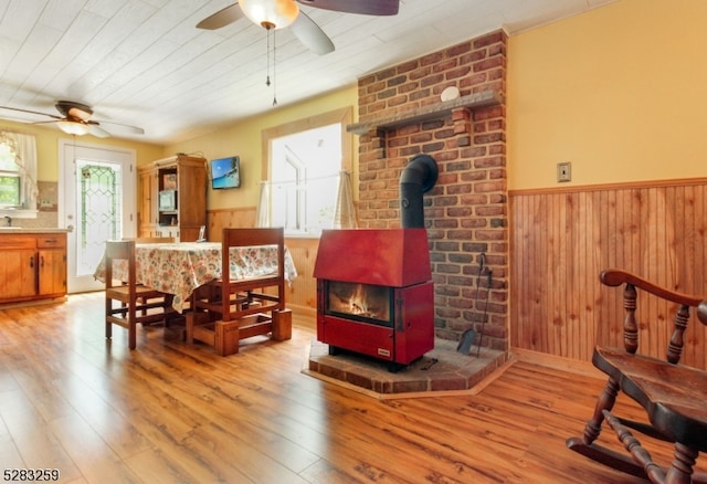 interior space featuring ceiling fan, sink, hardwood / wood-style flooring, a wood stove, and wood walls