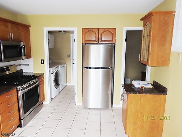 kitchen with dark stone countertops, light tile patterned floors, stainless steel appliances, and independent washer and dryer