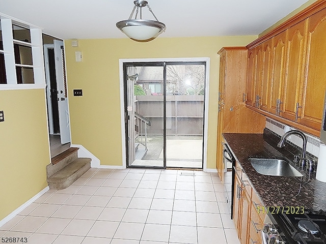 kitchen with dark stone counters, gas stove, sink, light tile patterned floors, and dishwasher