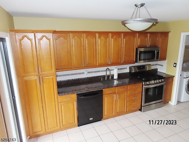 kitchen featuring stainless steel appliances, sink, dark stone countertops, washer / clothes dryer, and light tile patterned flooring