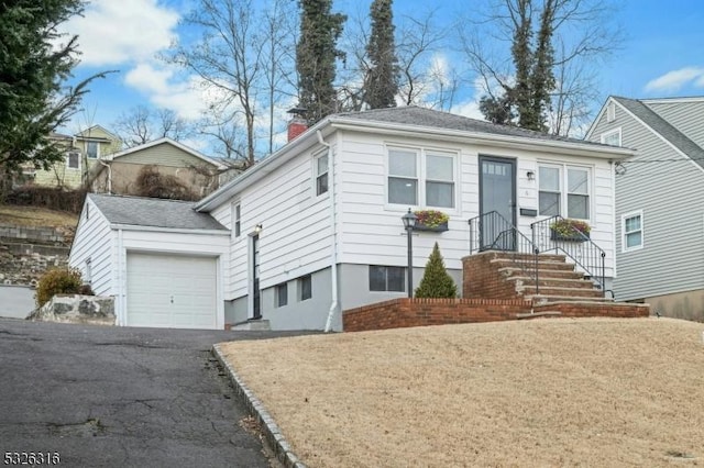 view of front facade with an attached garage, a chimney, and aphalt driveway