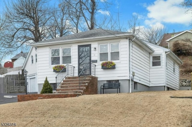 bungalow with driveway, a garage, fence, and a front yard