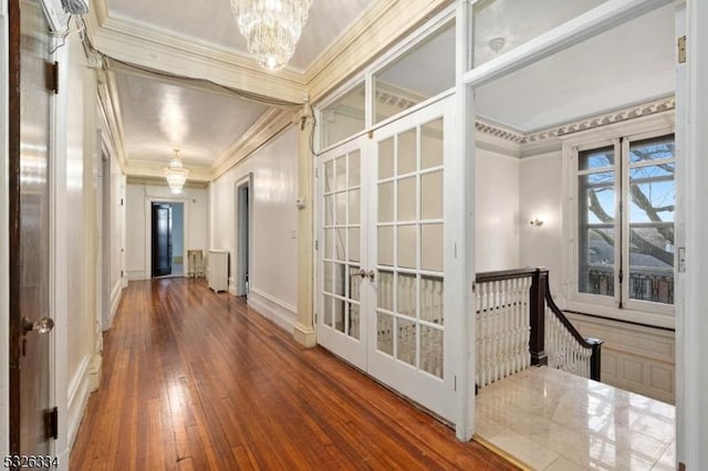 hallway featuring french doors, ornamental molding, wood-type flooring, a notable chandelier, and radiator heating unit