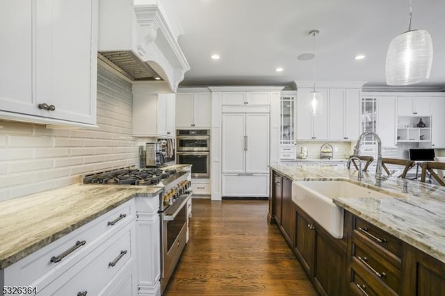 kitchen with premium range hood, premium appliances, sink, decorative light fixtures, and white cabinetry