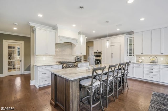 kitchen featuring a center island with sink, decorative light fixtures, white cabinetry, and a breakfast bar