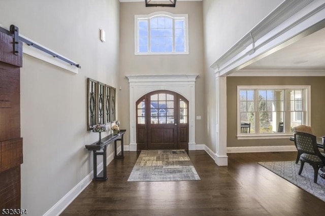 entrance foyer with a barn door, dark hardwood / wood-style flooring, a towering ceiling, and crown molding