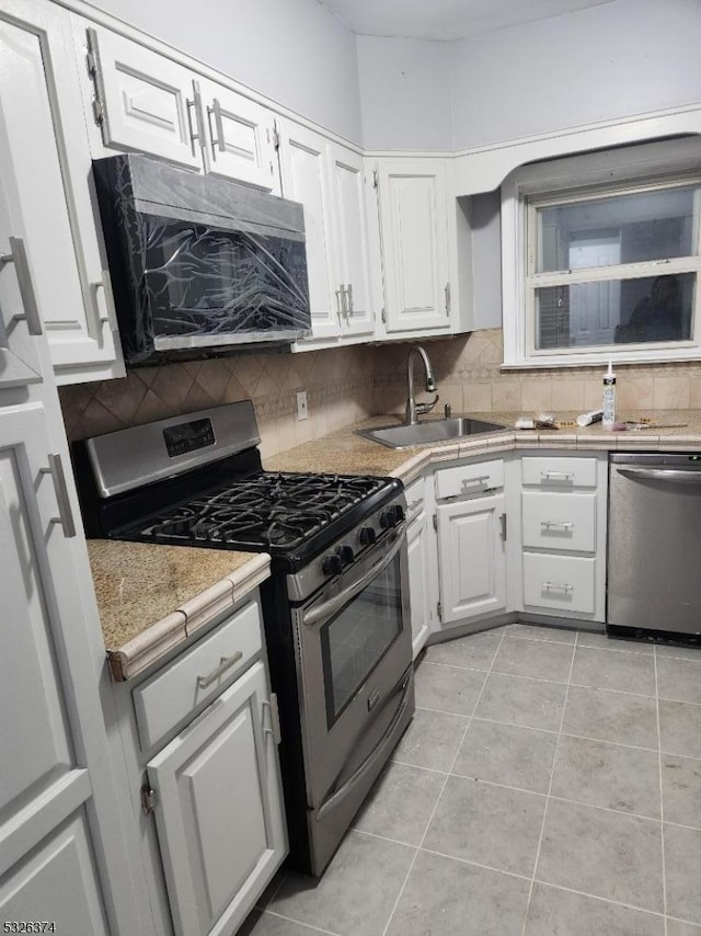 kitchen with sink, appliances with stainless steel finishes, tasteful backsplash, light tile patterned flooring, and white cabinetry