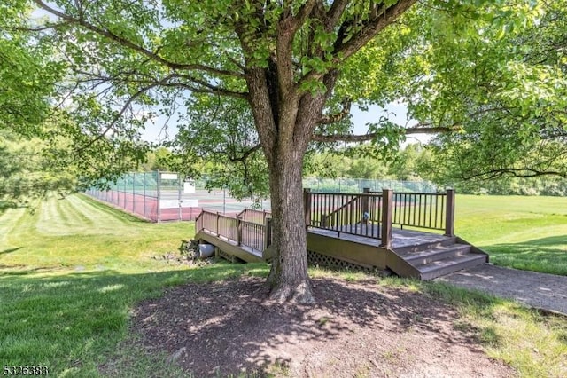 view of community with a tennis court, a lawn, fence, and a wooden deck