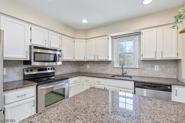 kitchen featuring a sink, appliances with stainless steel finishes, white cabinets, and dark stone countertops