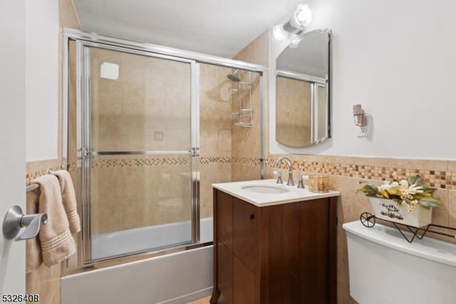 full bathroom featuring vanity, toilet, bath / shower combo with glass door, and tile walls