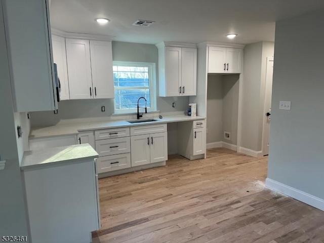 kitchen with white cabinetry, sink, and light wood-type flooring