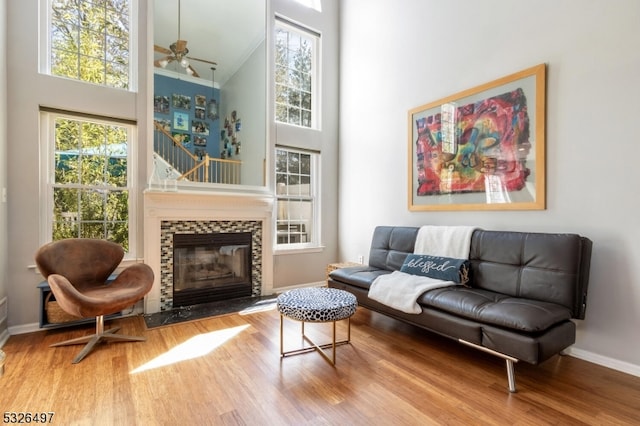 interior space featuring a towering ceiling, ceiling fan, wood-type flooring, and a tiled fireplace