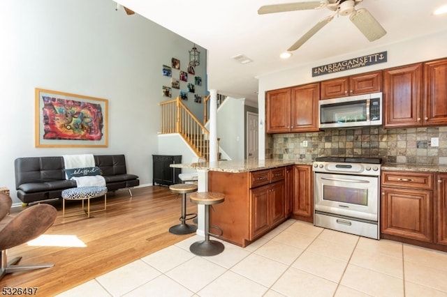 kitchen with kitchen peninsula, backsplash, light tile patterned floors, and appliances with stainless steel finishes