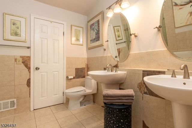 bathroom with toilet, dual sinks, tile walls, and tile patterned flooring