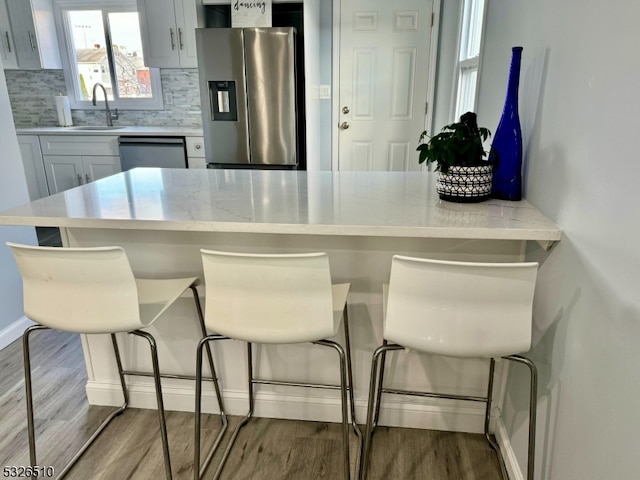 kitchen with sink, light wood-type flooring, appliances with stainless steel finishes, tasteful backsplash, and a kitchen bar