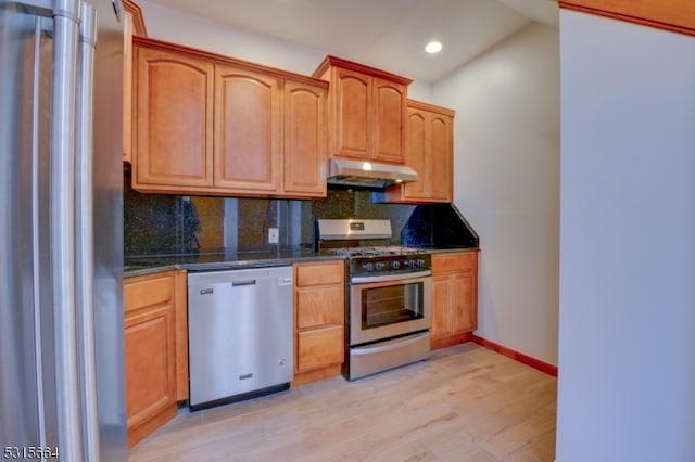 kitchen with lofted ceiling, dark stone counters, appliances with stainless steel finishes, tasteful backsplash, and light hardwood / wood-style floors