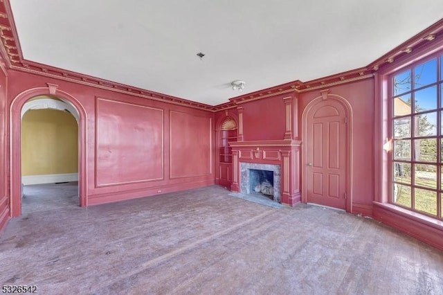 unfurnished living room featuring a premium fireplace, crown molding, carpet floors, and a healthy amount of sunlight