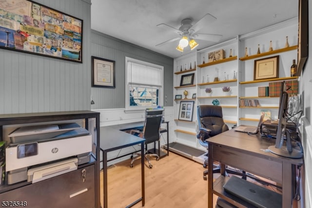 office area with light hardwood / wood-style floors, ceiling fan, and wood walls