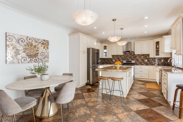 kitchen featuring sink, stainless steel appliances, wall chimney range hood, pendant lighting, and a kitchen island