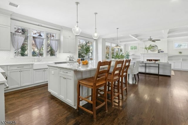 kitchen with sink, hanging light fixtures, a kitchen island, light stone countertops, and decorative backsplash