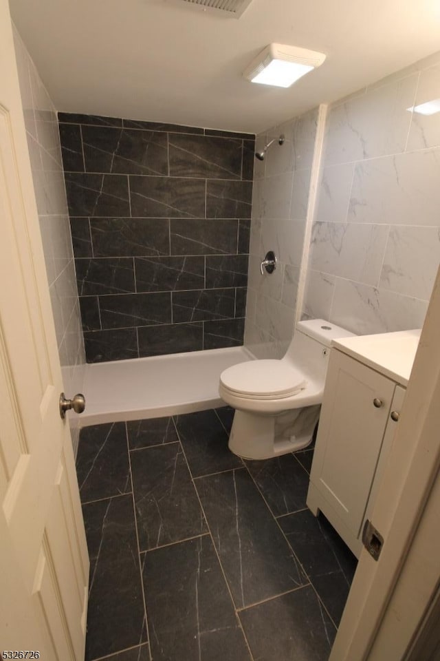 bathroom featuring a tile shower, vanity, toilet, and tile walls