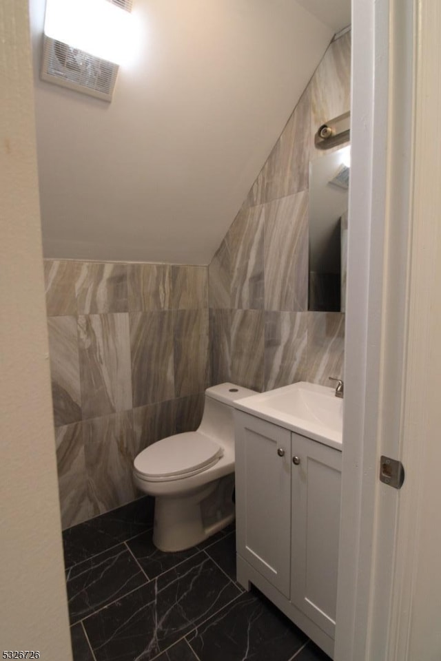 bathroom featuring vanity, toilet, tile walls, and lofted ceiling