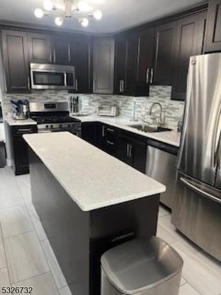 kitchen with sink, light tile patterned floors, tasteful backsplash, a kitchen island, and appliances with stainless steel finishes