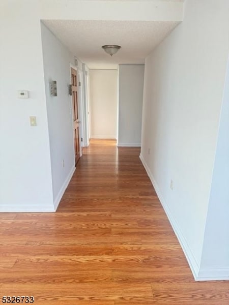 hallway with a textured ceiling and light hardwood / wood-style flooring