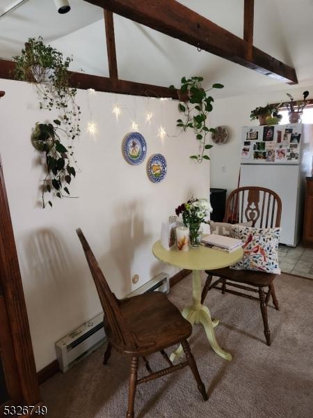 carpeted dining space featuring lofted ceiling with beams and a baseboard heating unit