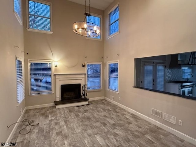 unfurnished living room featuring sink, a towering ceiling, a notable chandelier, and hardwood / wood-style flooring