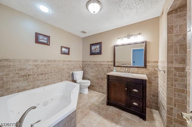 bathroom with a textured ceiling, vanity, toilet, and tile walls