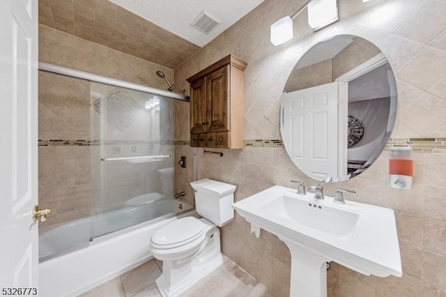 full bathroom featuring sink, enclosed tub / shower combo, tile patterned floors, toilet, and tile walls