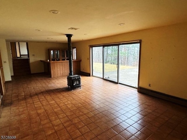 unfurnished living room with tile patterned flooring, a wood stove, and a baseboard heating unit