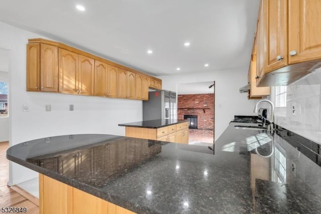 kitchen featuring kitchen peninsula, a brick fireplace, sink, light hardwood / wood-style flooring, and dark stone countertops