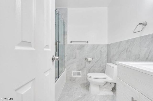 full bathroom with vanity, enclosed tub / shower combo, tile walls, and toilet