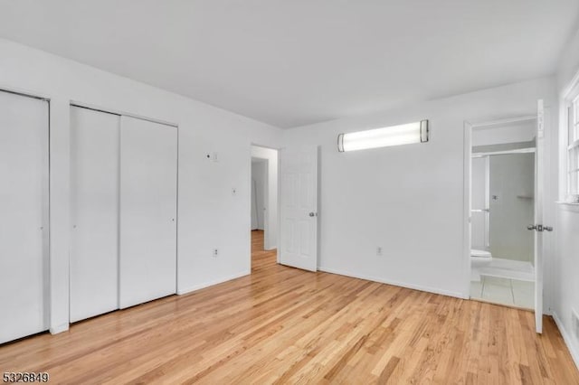 unfurnished bedroom featuring light hardwood / wood-style floors, ensuite bath, and multiple closets