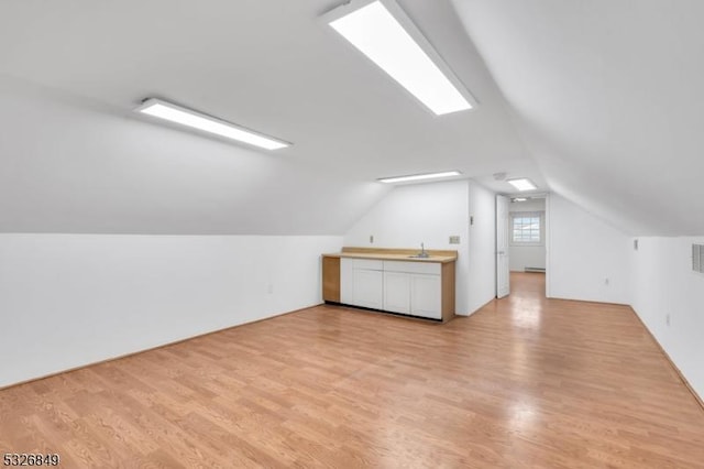 additional living space with sink, light hardwood / wood-style floors, and vaulted ceiling