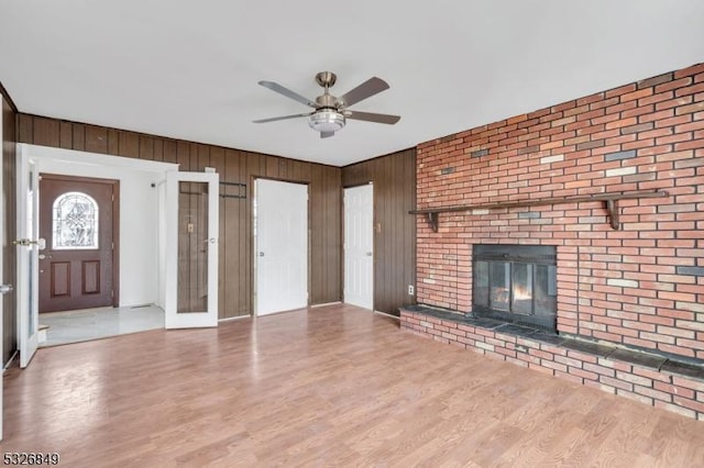 unfurnished living room with hardwood / wood-style flooring, a brick fireplace, and wood walls